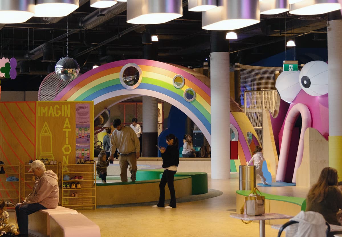 Families playing inside Imaginationation, seen through the rainbow archway entrance